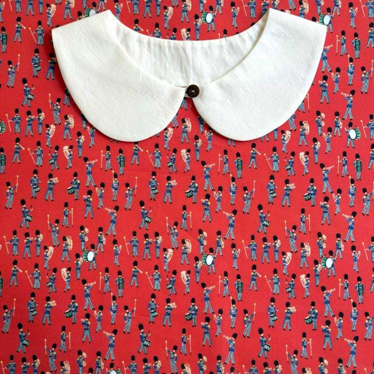 a white collar with a button, placed on a red fabric with a repeating pattern of soldiers marching in formation.