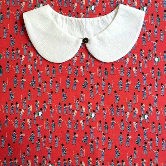 a white collar with a button, placed on a red fabric with a repeating pattern of soldiers marching in formation.
