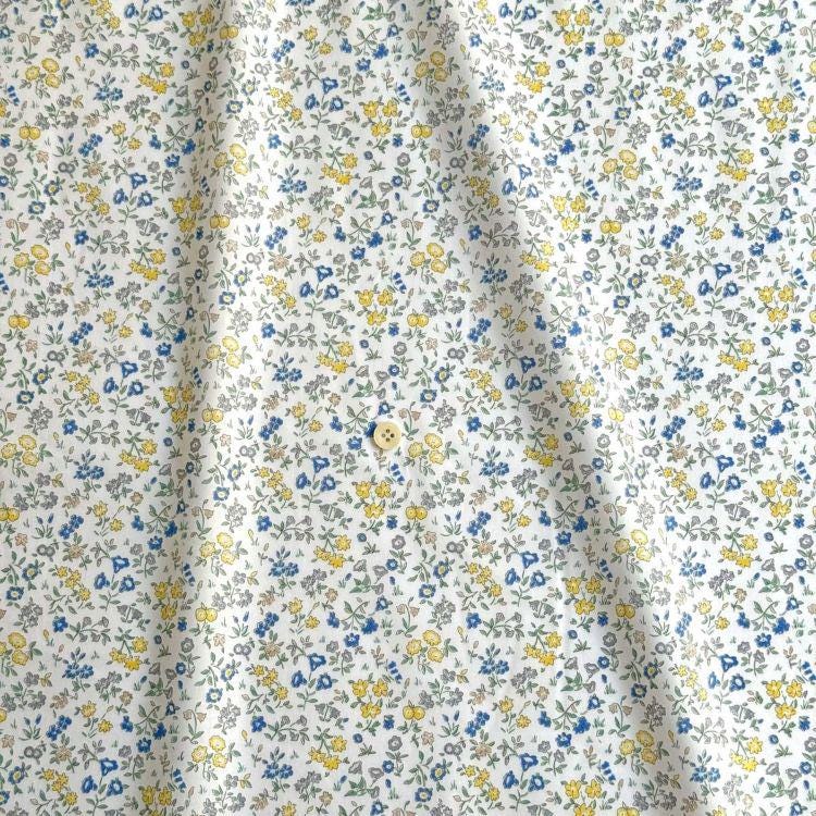 a close-up view of a fabric with a floral pattern in shades of yellow and blue. The fabric appears to be made of a soft, white material, and there is a small button visible in the center of the pattern.