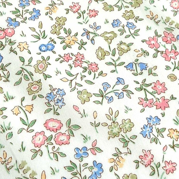 a close-up view of a fabric with a floral pattern. The fabric is adorned with various types of flowers, including pink, blue, and green flowers, as well as leaves and stems. The flowers are arranged in a scattered manner, creating a visually appealing and intricate design. The image does not contain any text or specific details about the objects or their arrangement.