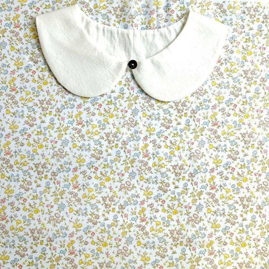 a white collar with a black button, set against a background of a floral print fabric.