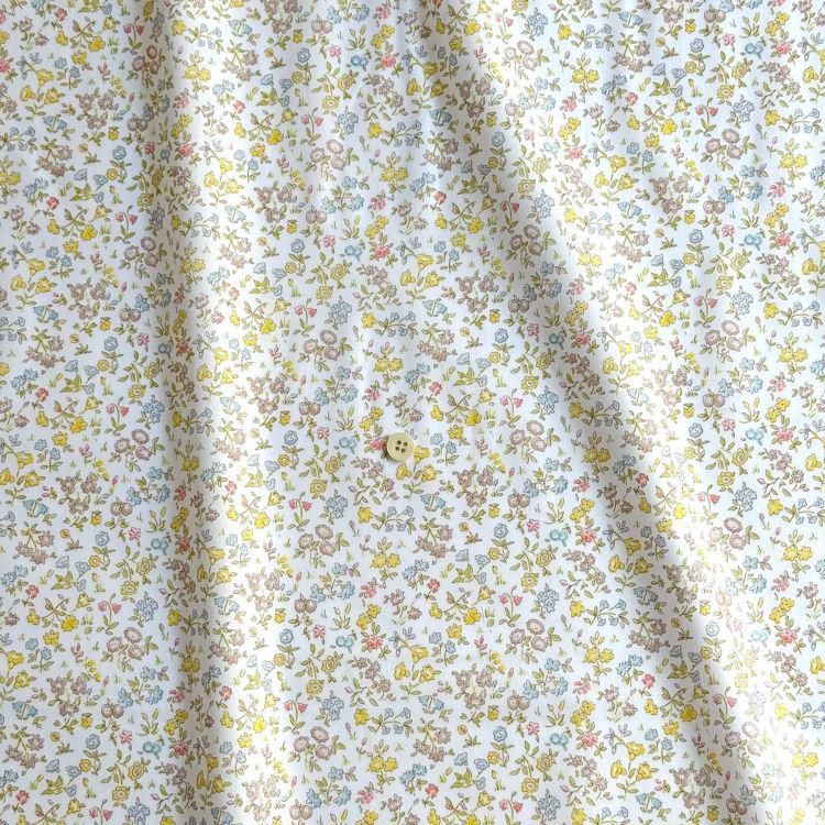 a close-up view of a fabric with a floral pattern in shades of yellow, white, and blue. The fabric appears to be made of cotton and has a slight crease visible on the left side. There is a small button visible in the center of the fabric.