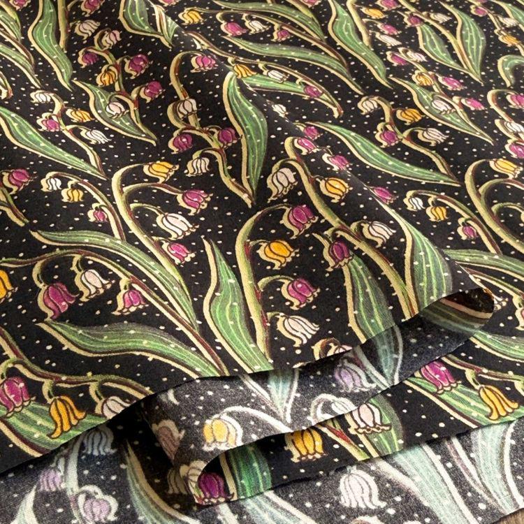 a close-up view of a fabric with a repeating pattern of green leaves and pink flowers against a black background.