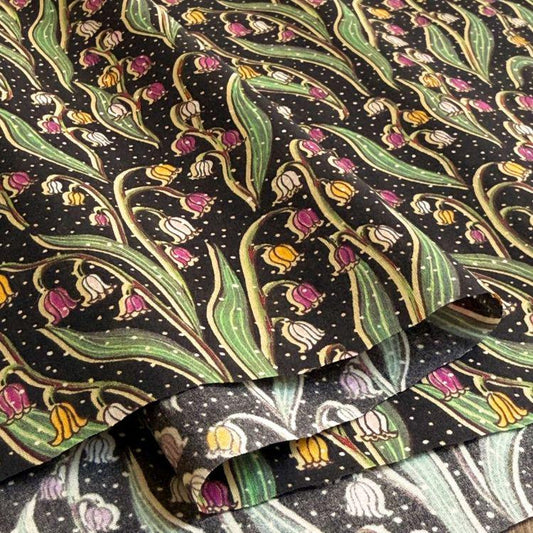 a close-up view of a fabric with a repeating pattern of green leaves and pink flowers against a black background.