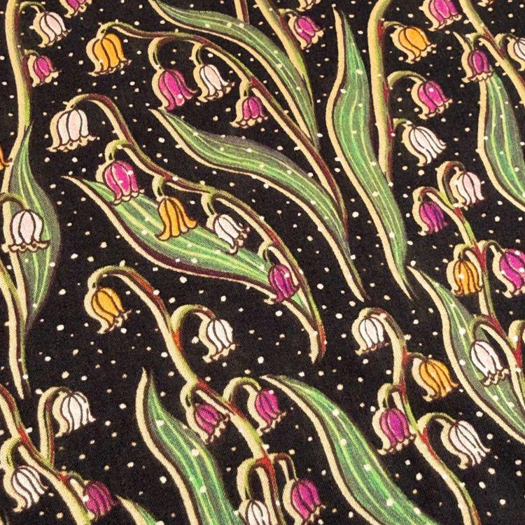 a close-up view of a patterned fabric with a repeating design of lily of the valley flowers. The flowers are depicted in various colors, including pink, yellow, and green, and are arranged in a repeating pattern across the fabric. The background of the fabric is dark, providing a contrast that makes the colorful flowers stand out.
