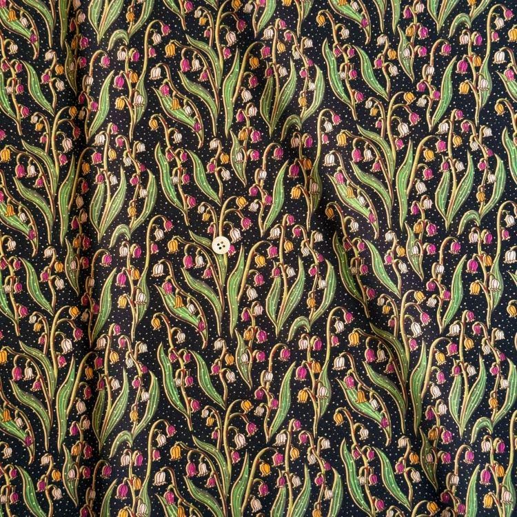 a close-up view of a fabric with a repeating pattern of green leaves and pink flowers against a dark background.