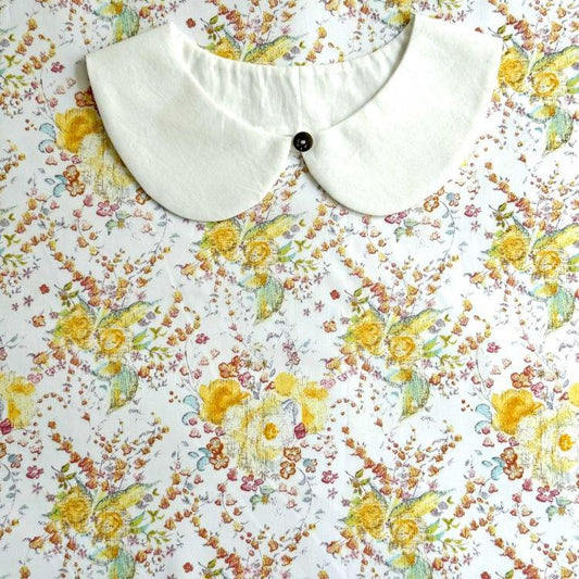 a white collar with a black button, set against a background with a floral print.
