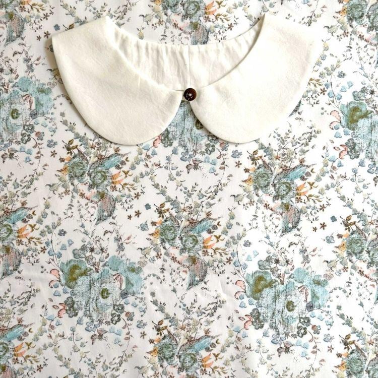 a white collar with a button, set against a floral print background.