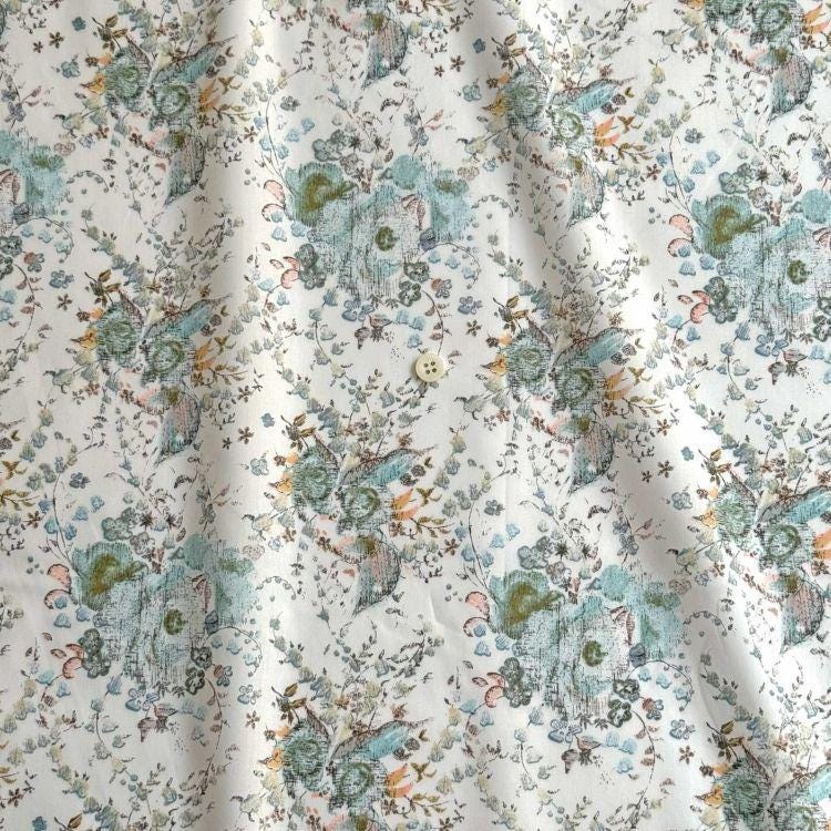 a close-up view of a fabric with a floral pattern. The fabric appears to be white and features a repeating pattern of flowers and leaves in shades of green, blue, and orange. The pattern is intricate and detailed, creating a visually appealing design.