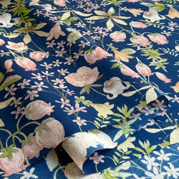 a close-up view of a fabric with a floral pattern in shades of blue and pink. The pattern consists of various flowers and leaves, creating a visually appealing and intricate design.