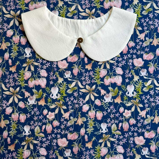 a white collar with a button, placed on a blue fabric with a floral pattern.