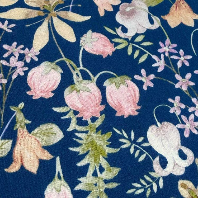a close-up view of a fabric with a floral pattern. The fabric is predominantly blue, with various pink and white flowers and leaves scattered across it. The flowers and leaves appear to be the main focus of the image, creating a visually appealing and intricate design.