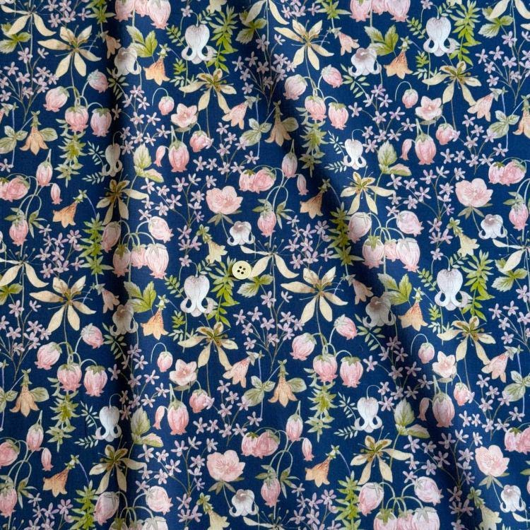 a close-up view of a fabric with a floral pattern in shades of blue and pink. The pattern consists of various flowers, leaves, and other natural elements arranged in a repeating design. The fabric appears to be made of a material that resembles cotton or linen, and the colors are vibrant and eye-catching.
