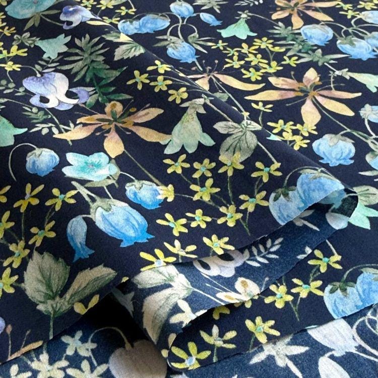 a close-up view of a fabric with a floral pattern. The fabric appears to be dark blue, and it is adorned with various flowers and leaves in shades of yellow and green. The pattern is intricate and detailed, showcasing the craftsmanship of the fabric.