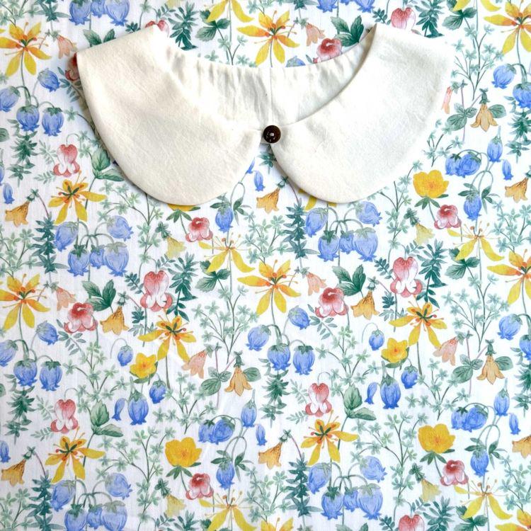 a white collar with a button, placed on a fabric with a colorful floral pattern.