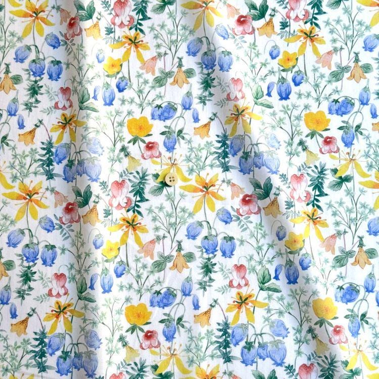 The image is a vibrant and colorful fabric with a repeating pattern of various flowers and leaves in shades of yellow, blue, and green. The pattern is intricate and detailed, creating a visually appealing and lively design.