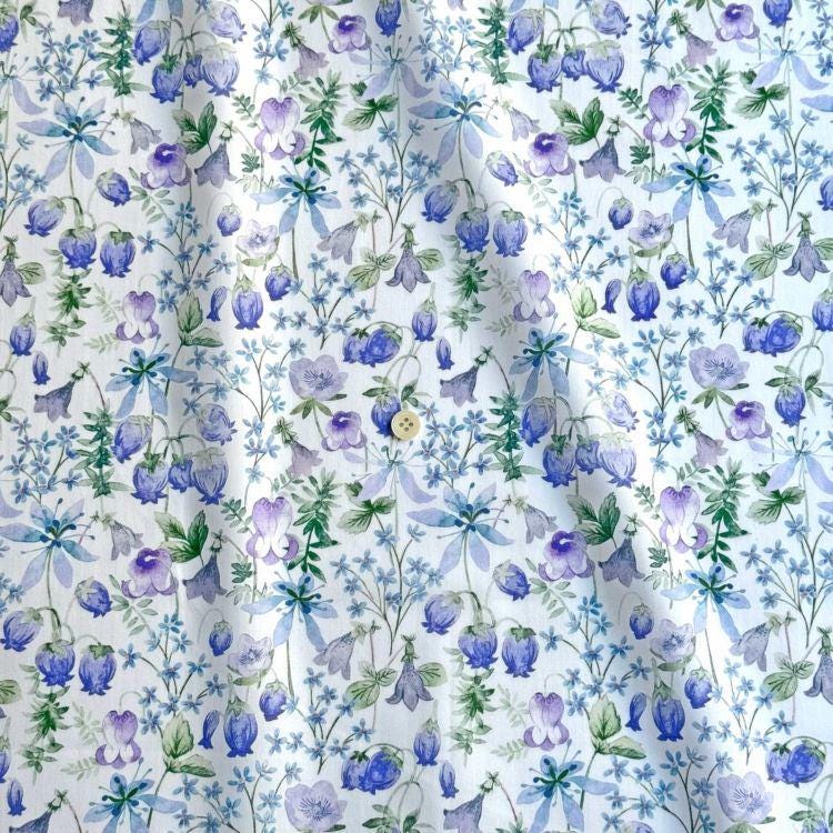 a close-up view of a fabric with a repeating pattern of blue and green flowers and leaves. The pattern is intricate and detailed, with the flowers and leaves varying in size and shape. The fabric appears to be made of a soft, delicate material, suitable for clothing or home decor.