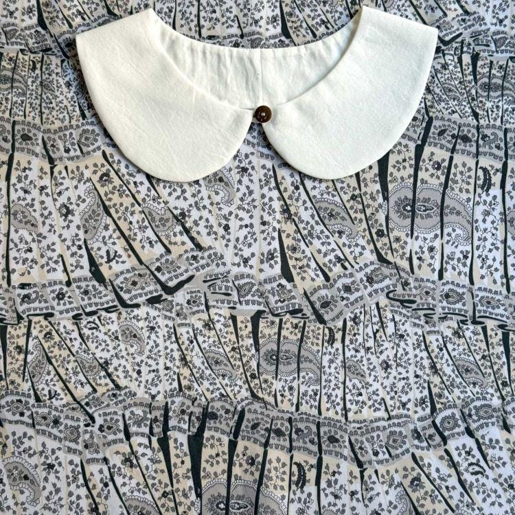 a white collar with a button, placed on a patterned fabric with a repeating black and white design.