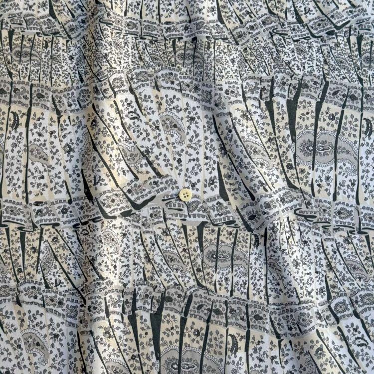 The image is a close-up view of a fabric with a repeating pattern of black and white designs, including floral and geometric motifs. The fabric appears to be made of a soft, textured material, and there is a small button visible in the center of the pattern.