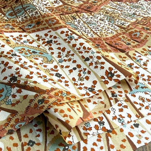 The image is a close-up view of a fabric with a repeating pattern of leaves and flowers in various shades of brown, orange, and white. The pattern is intricate and detailed, creating a visually appealing and textured surface.