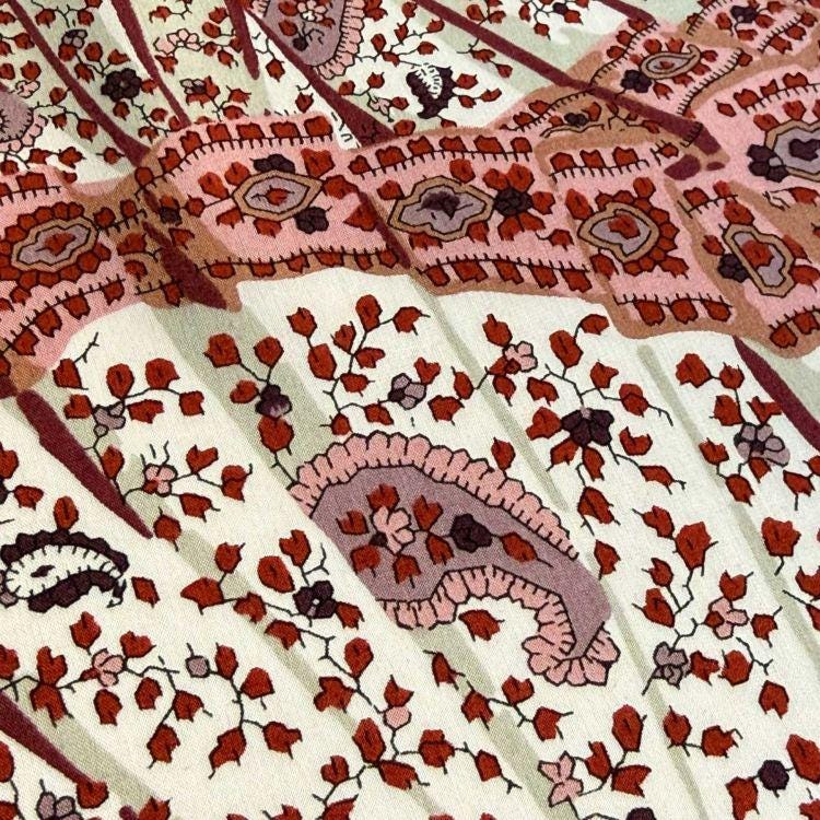 a close-up view of a fabric with a floral pattern in shades of pink, red, and white. The pattern is intricate and detailed, with various shapes and designs that create a visually appealing and textured appearance.