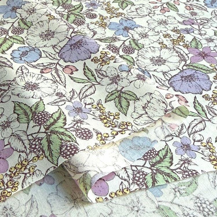 a close-up view of a fabric with a floral pattern. The pattern consists of various flowers and leaves in different colors, including white, purple, and green. The fabric appears to be a piece of paper or fabric with a printed design.