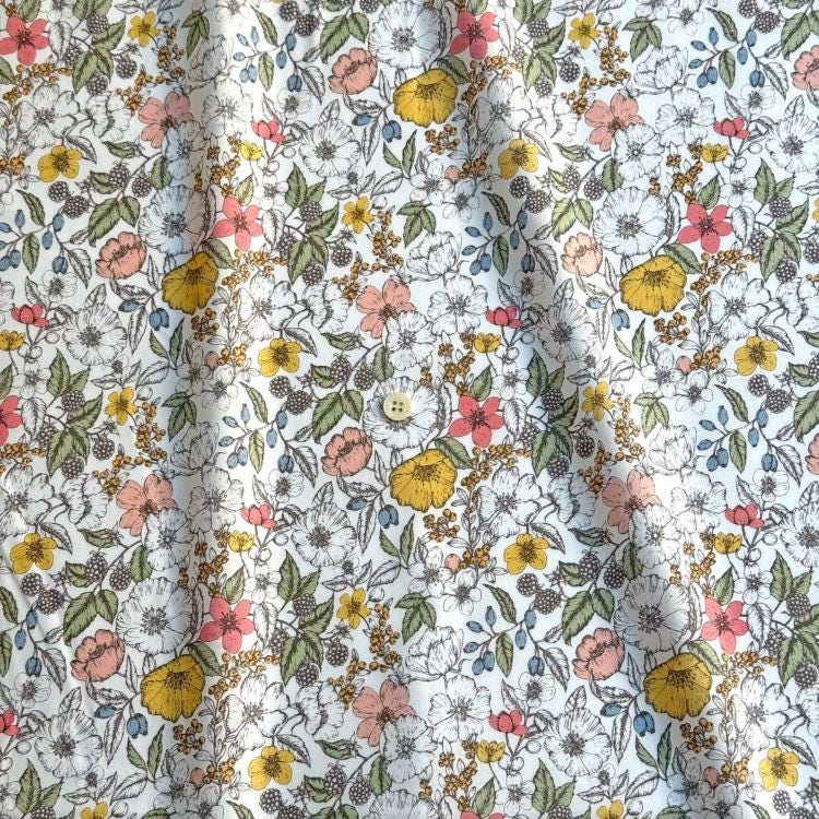 a close-up view of a fabric with a floral pattern. The fabric is predominantly white, with various colorful flowers and leaves scattered across it. The pattern includes a mix of pink, yellow, and green flowers, as well as leaves and berries. The fabric appears to be made of a soft, textured material, suitable for clothing or home decor.