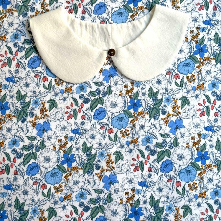 a white collar with a button, placed on a fabric with a floral pattern of blue, white, and orange flowers.