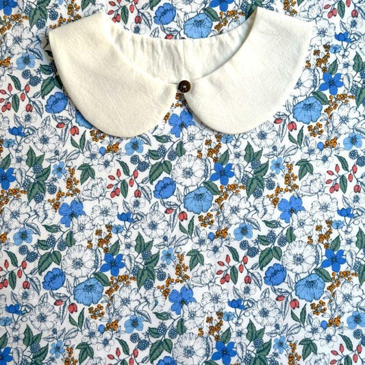 a white collar with a button, placed on a fabric with a floral pattern of blue, white, and orange flowers.