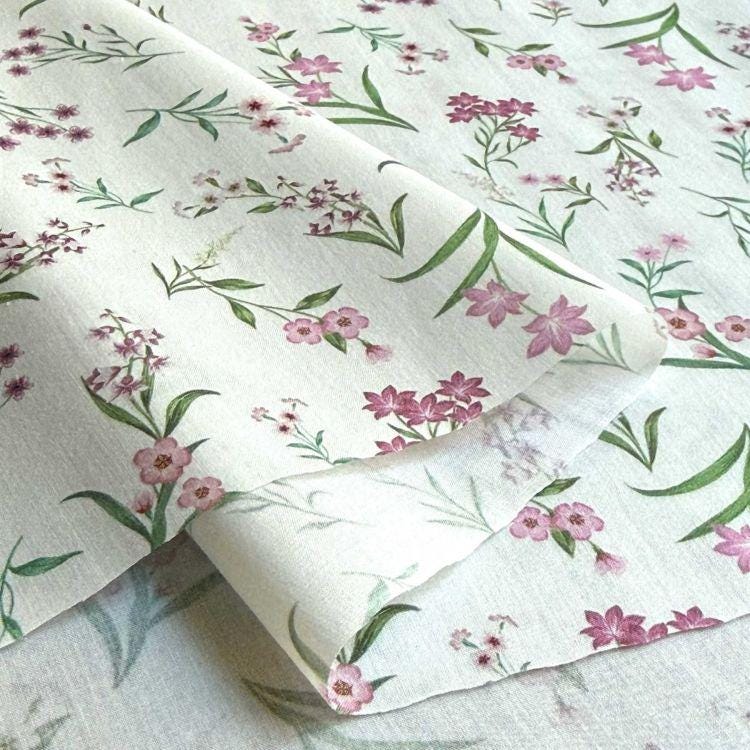 a close-up view of a fabric with a floral pattern, including pink flowers and green leaves. The fabric appears to be white, and the pattern is intricate and detailed.