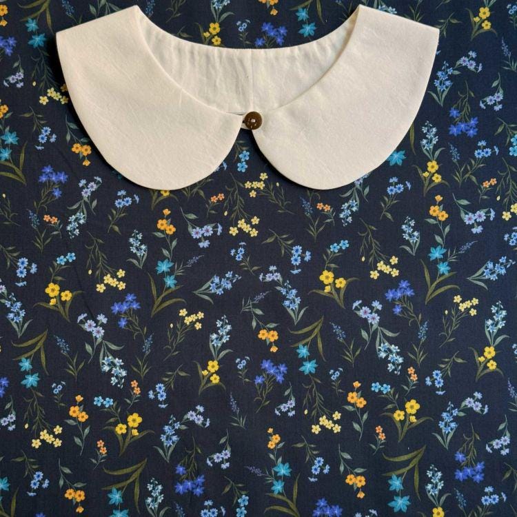 a white collar with a button, set against a background with a floral pattern in shades of blue, yellow, and orange.
