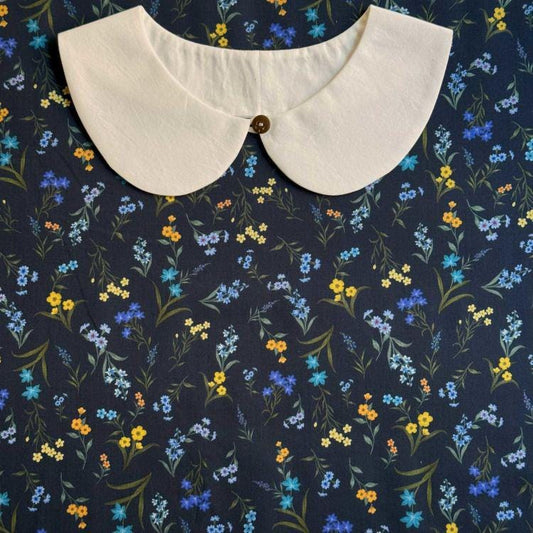 a white collar with a button, set against a background with a floral pattern in shades of blue, yellow, and orange.