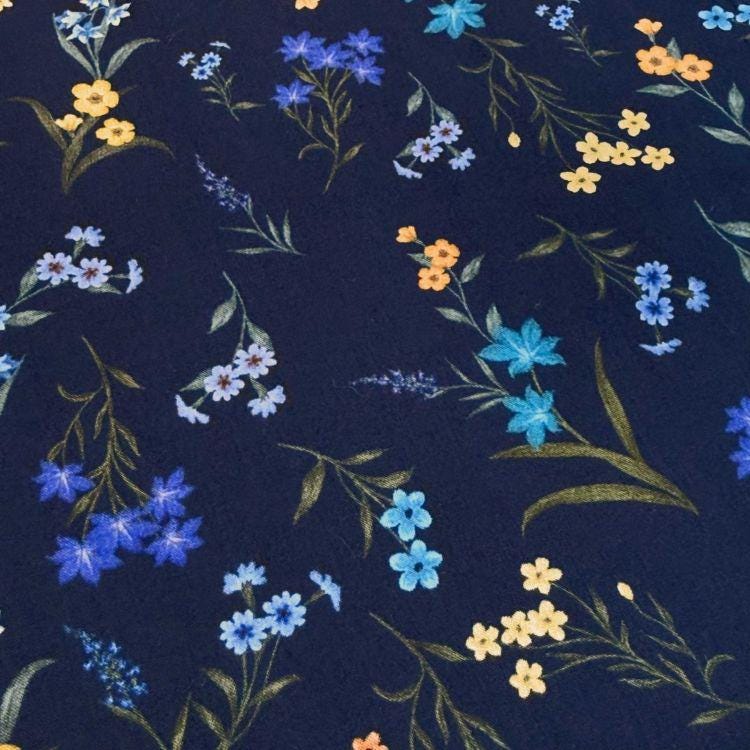 a close-up view of a dark blue fabric adorned with a variety of colorful flowers and leaves, including blue, yellow, and orange flowers. The flowers are arranged in a scattered pattern across the fabric, creating a visually appealing and vibrant design.