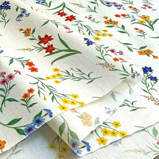 a close-up view of a fabric with a vibrant floral pattern. The fabric is predominantly white, adorned with a variety of colorful flowers and leaves in shades of red, orange, yellow, and blue. The pattern is intricate and detailed, showcasing the craftsmanship of the fabric.