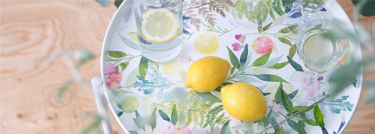 A white plate with a floral pattern holds two lemons and two glasses of water, placed on a wooden surface.