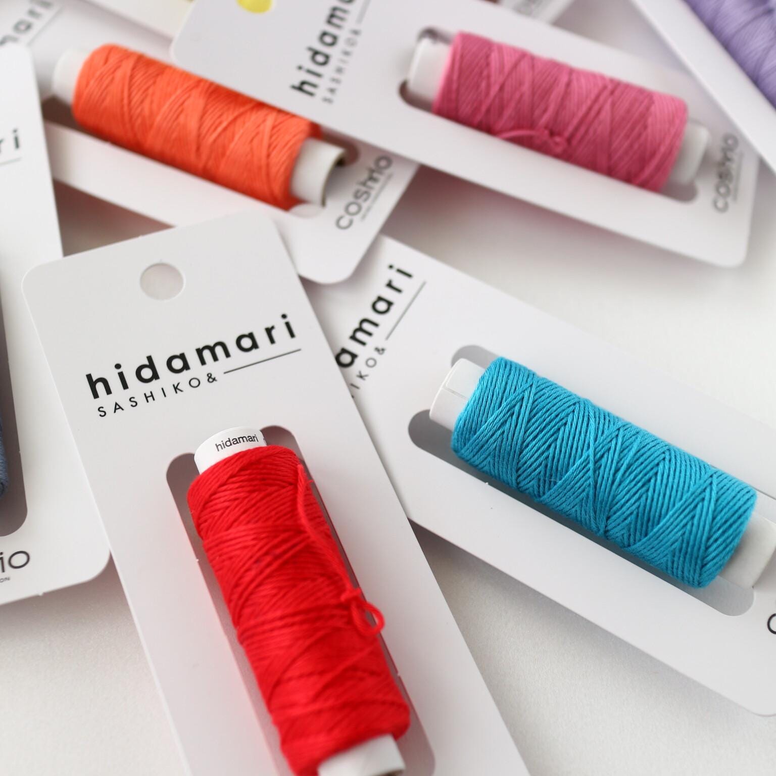 A close-up image of colorful spools of thread in packaging, with the brand name "hiddamari" printed on the packaging.