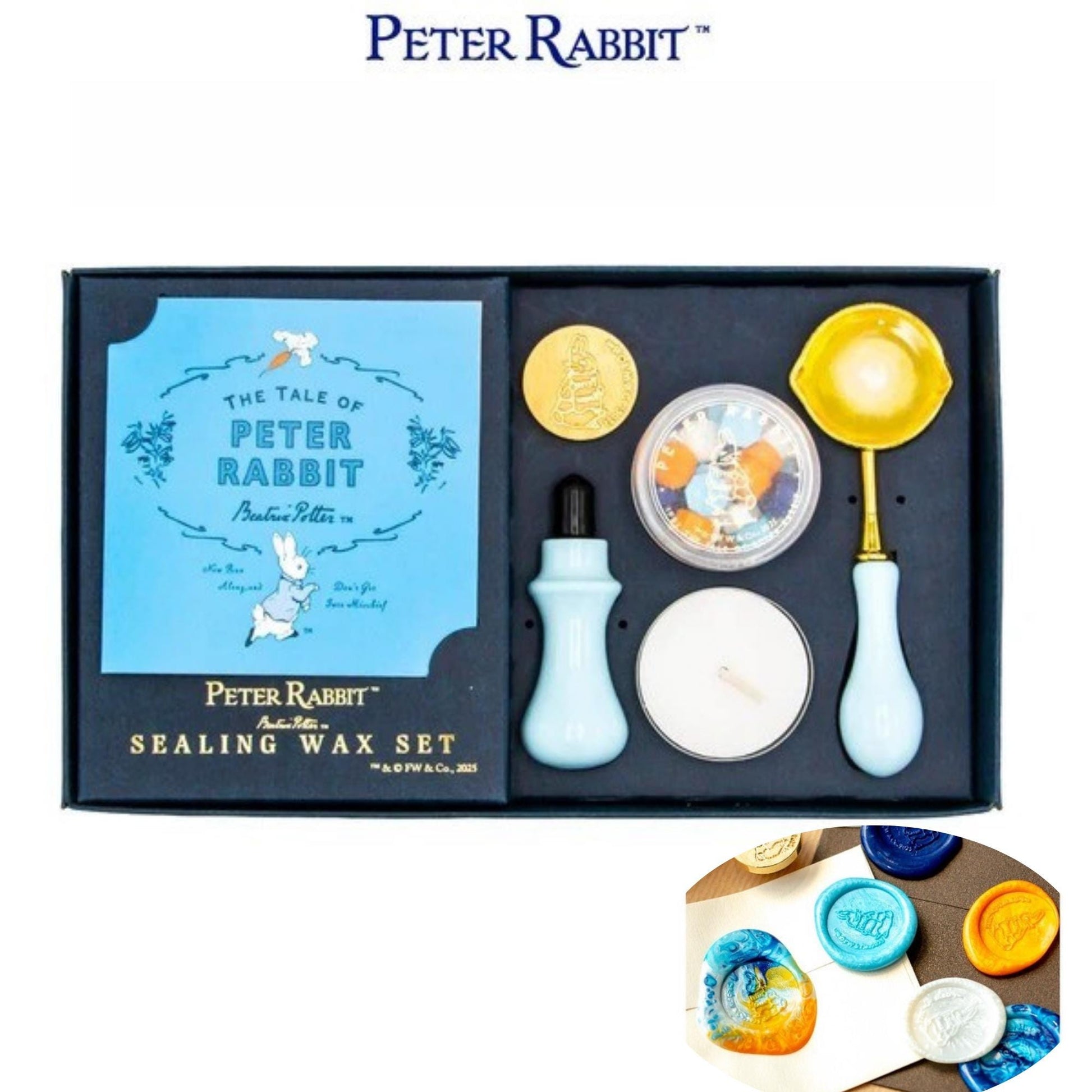 A set of Peter Rabbit themed sealing wax tools, including a blue book, a yellow container, and a white container, all displayed in a black box.