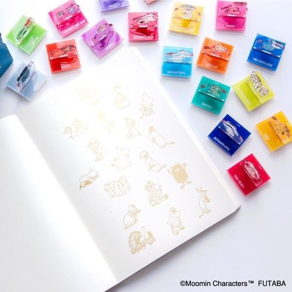 a white notebook with various colorful stickers or decals on the pages, as well as a collection of small, colorful objects scattered around the notebook.