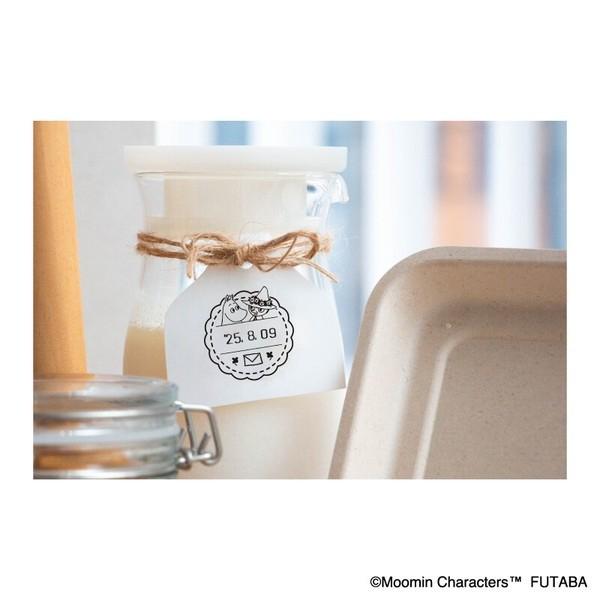 a close-up of a jar with a label, and there is a blurred background that includes a jar and a cardboard box.