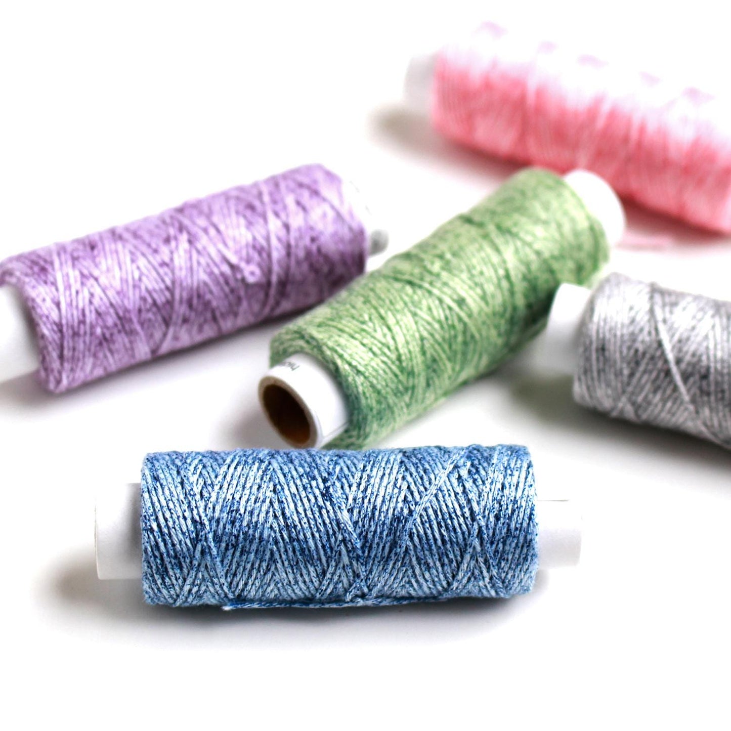 a collection of colorful spools of thread, including purple, green, blue, and pink, arranged on a white background.