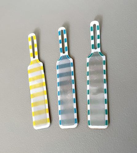 Three colorful paddle-shaped objects with yellow, blue, and white stripes are arranged in a row on a gray background.