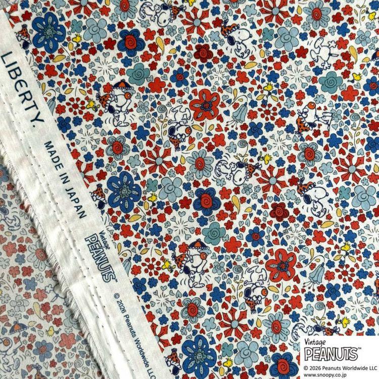 a vibrant and colorful fabric with a repeating pattern of flowers and Peanuts characters. The fabric appears to be a handmade piece, as indicated by the "Liberty" label. The fabric is printed with a variety of colors, including red, blue, and white, creating a visually appealing and lively design.