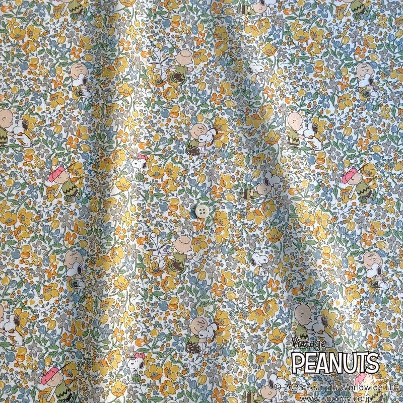 The image is a close-up of a fabric with a repeating pattern of cartoon characters, including Peanuts characters, such as Snoopy and Charlie Brown. The pattern consists of various shades of yellow, green, and orange, creating a vibrant and playful visual effect.