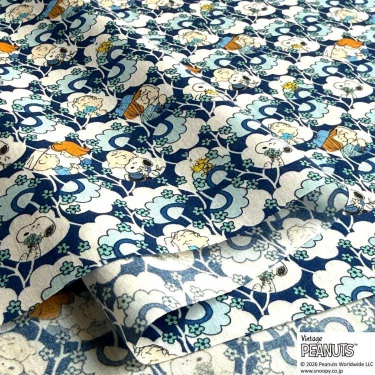 a close-up view of a fabric with a repeating pattern of cartoon characters, specifically the Peanuts characters. The pattern consists of various Peanuts characters, such as Snoopy, Woodstock, and Charlie Brown, arranged in a visually appealing and colorful manner. The fabric appears to be a piece of clothing or textile, with the repeating pattern creating a sense of depth and texture.
