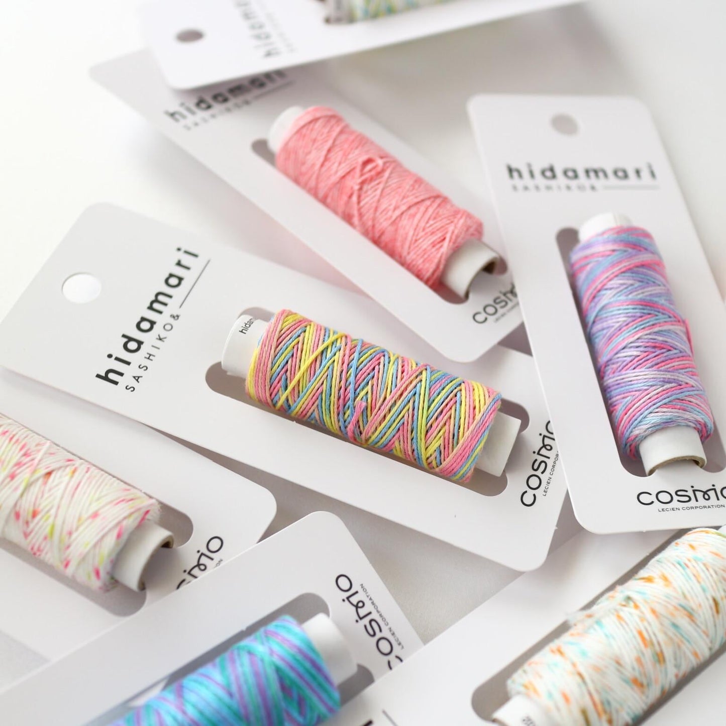 A collection of colorful spools of thread in various patterns, each attached to a white card with the brand name "hideamari" printed on it.