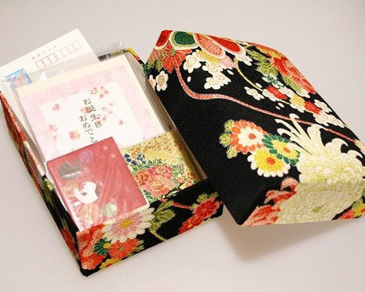 a decorative box with a floral pattern, containing various items such as a card, a small picture frame, and some other miscellaneous objects.