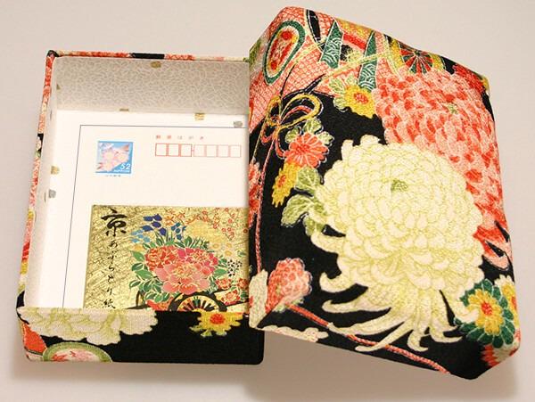an open box with a floral pattern on the lid and a card inside.