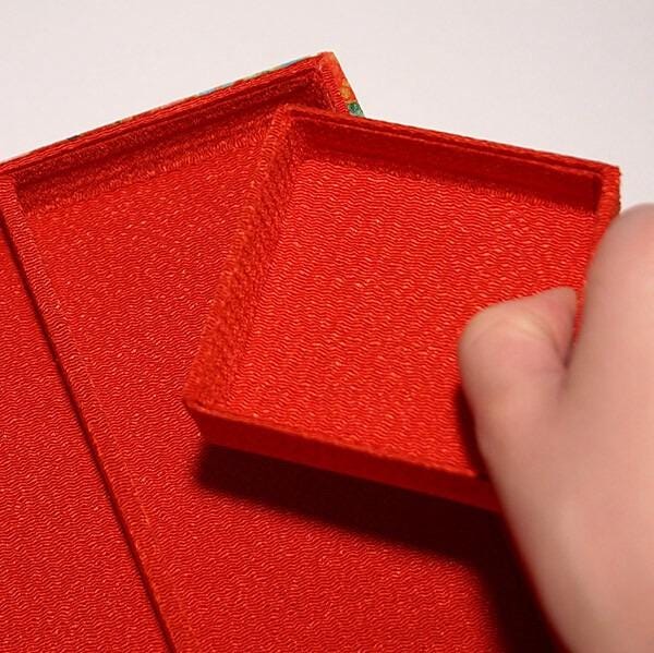 A hand is holding a red box with a visible pattern on it, against a plain white background.
