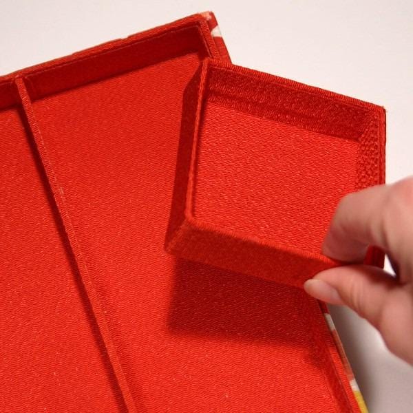 A hand is holding a red box with a matching lid, which is placed on a white surface.
