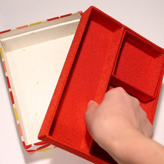 A hand is holding a red box with a white interior, which appears to be an open box.